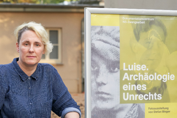 Die Comic-Zeichnerin Elke R. Steiner neben dem Plakat zur Ausstellung